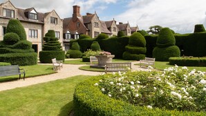 A historic stone building with a formal garden, manicured hedges, and a central seating area with benches.
