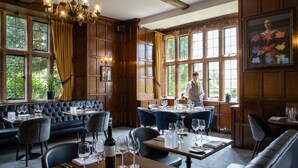 A restaurant with wooden paneling, large windows, and a chandelier. Tables are set with wine glasses and plates.