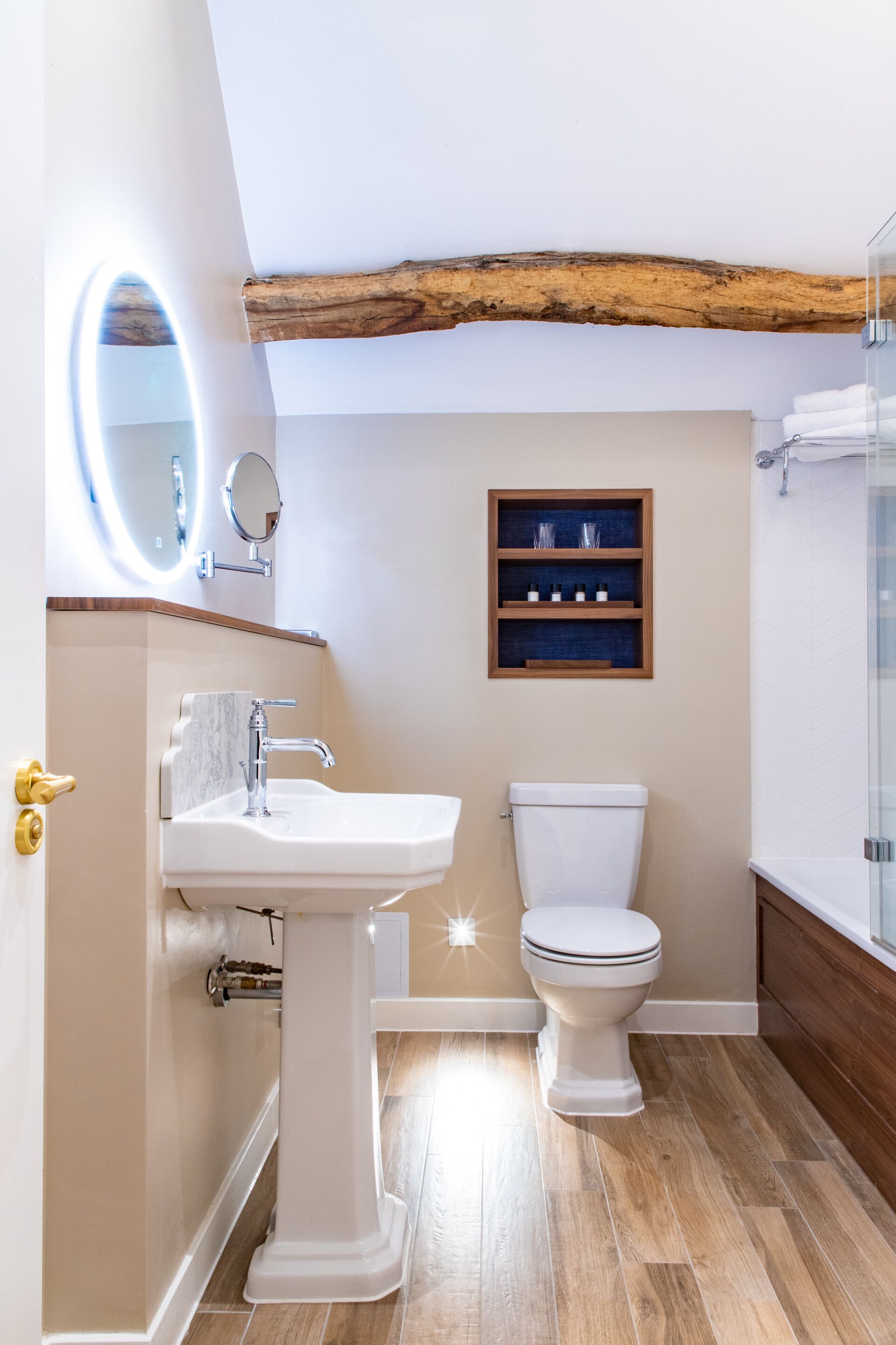A bathroom with a pedestal sink, a toilet, a wooden shelf with toiletries, and a mirror.