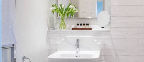 Une salle de bain avec un lavabo blanc, un miroir et une baignoire. On y trouve un porte-serviettes avec des serviettes et un vase avec des fleurs sur le lavabo.