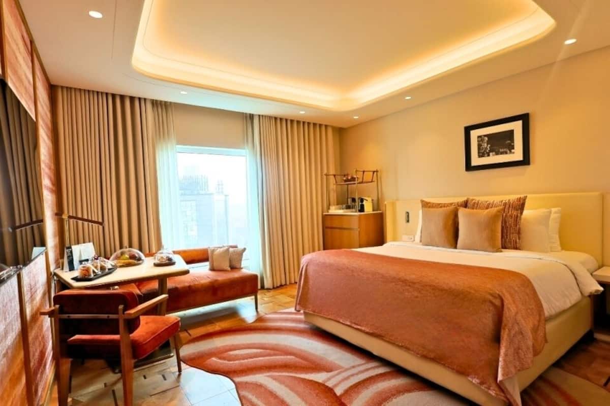 A hotel room with a bed, a desk with a chair, a nightstand, and a window with curtains.