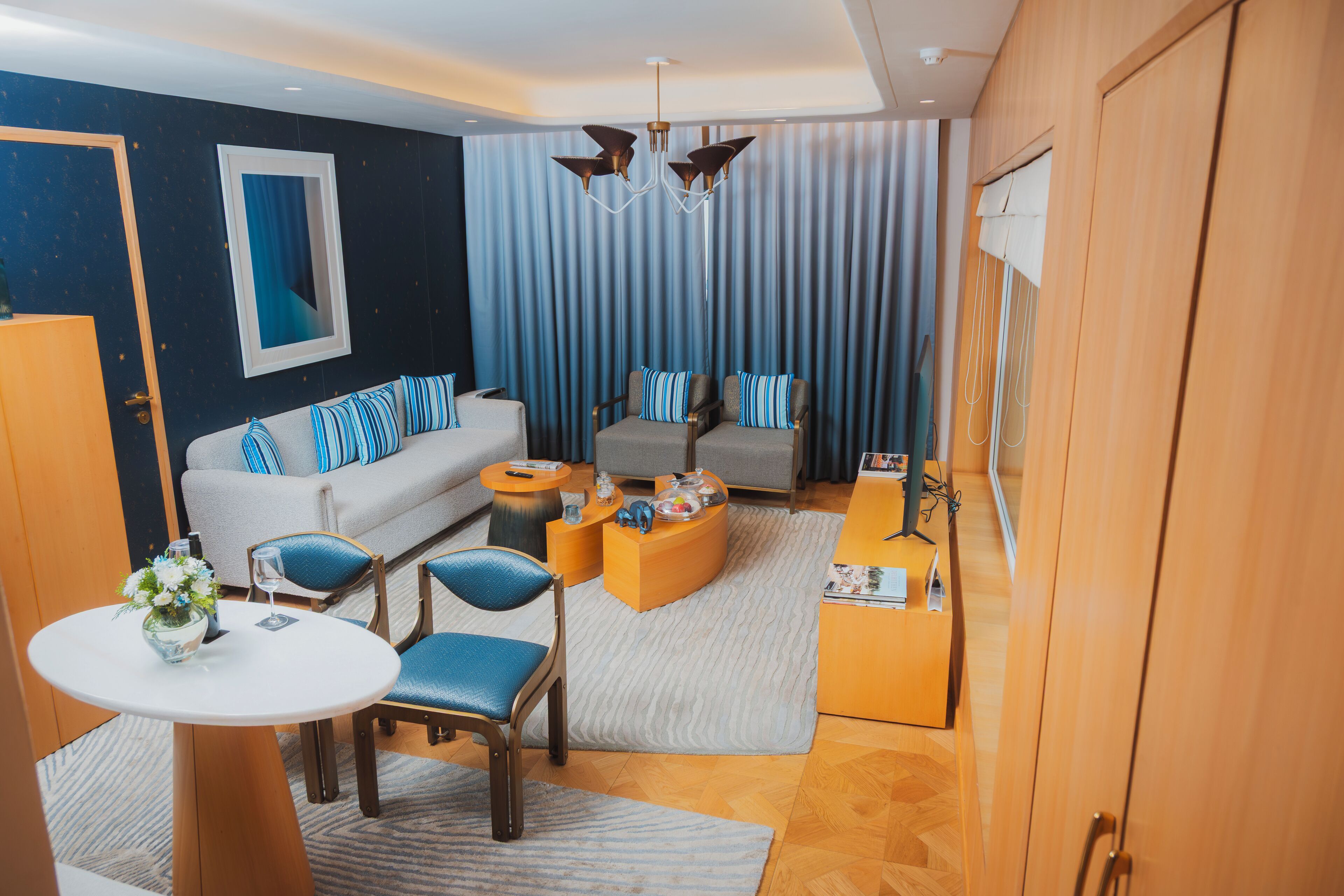 A modern hotel room with a sofa, armchairs, a coffee table, and a small table with a vase of flowers.