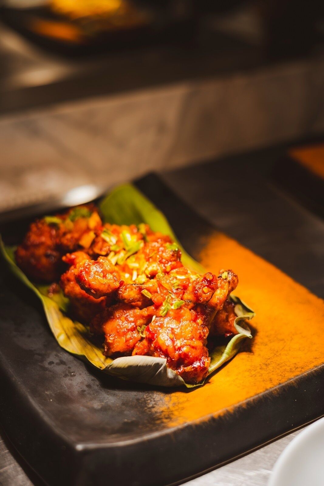 A dish of fried chicken on a banana leaf served on a black plate.
