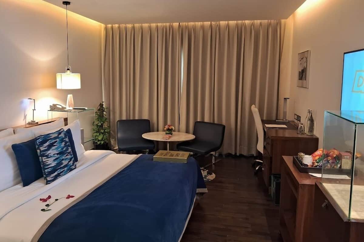 A hotel room with a bed, bedside table, lamp, chair, desk, and a television.