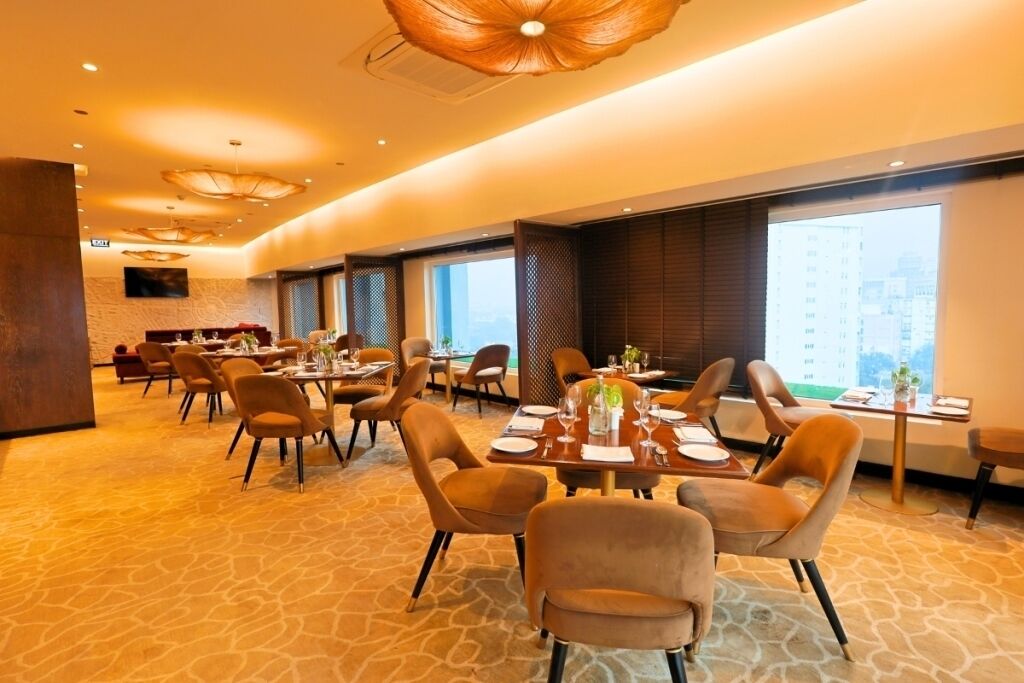 A hotel dining area with multiple tables and chairs, large windows, and a modern interior design.