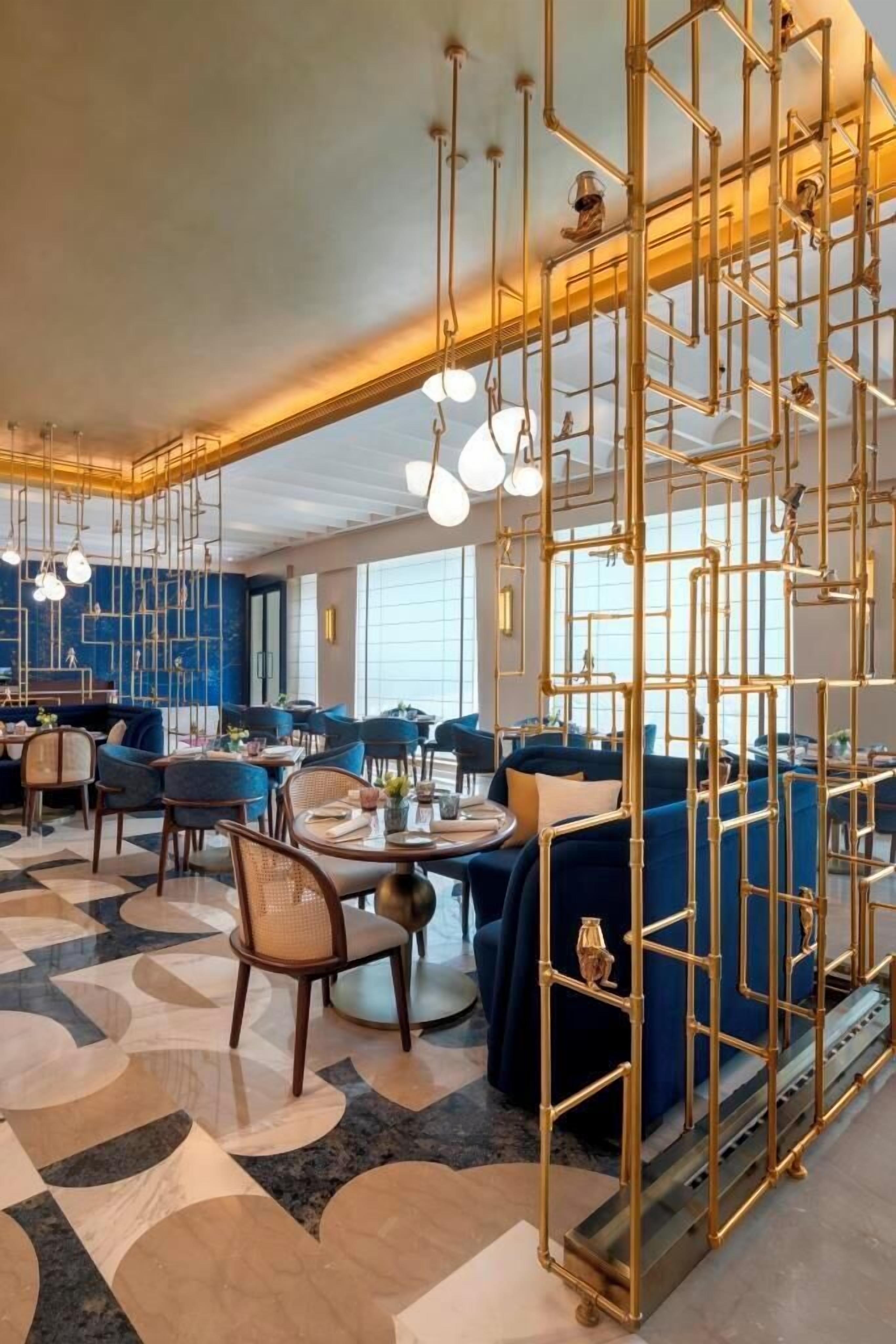A modern hotel lobby with a geometric floor pattern, blue seating, and a decorative metal partition.