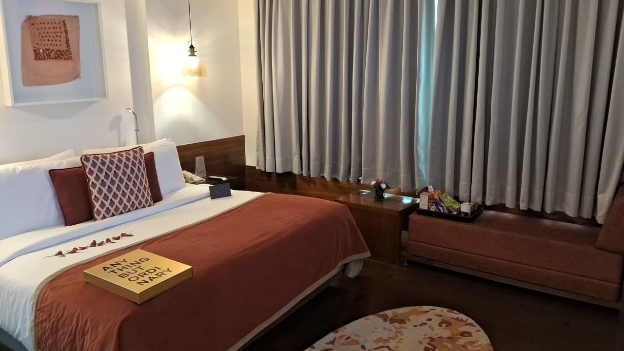 A hotel room with a bed, a nightstand, a chair, and a window with curtains.