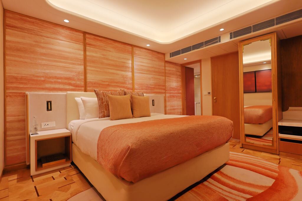 A modern hotel room with a large bed, wooden panel walls, a nightstand, and a mirror.