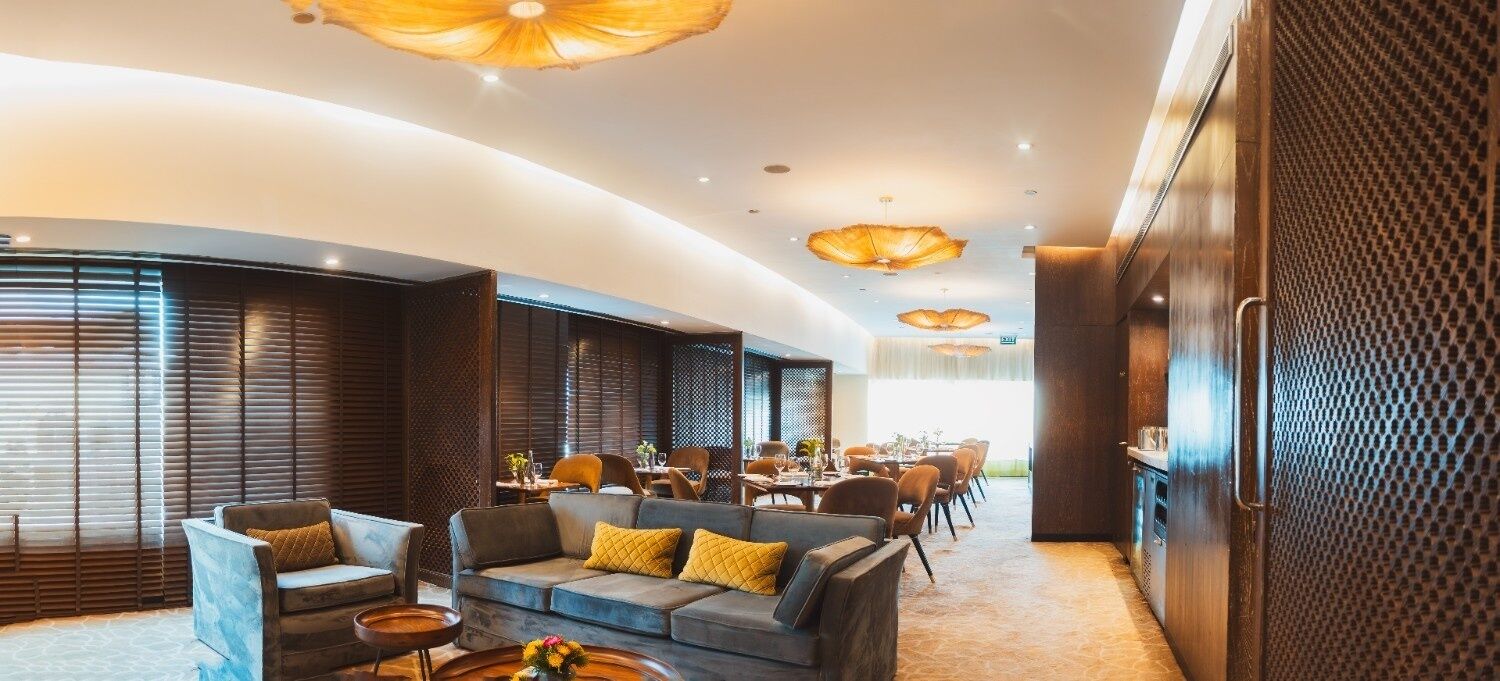 A modern hotel lobby with a curved ceiling, wooden paneling, and a seating area with sofas and chairs.