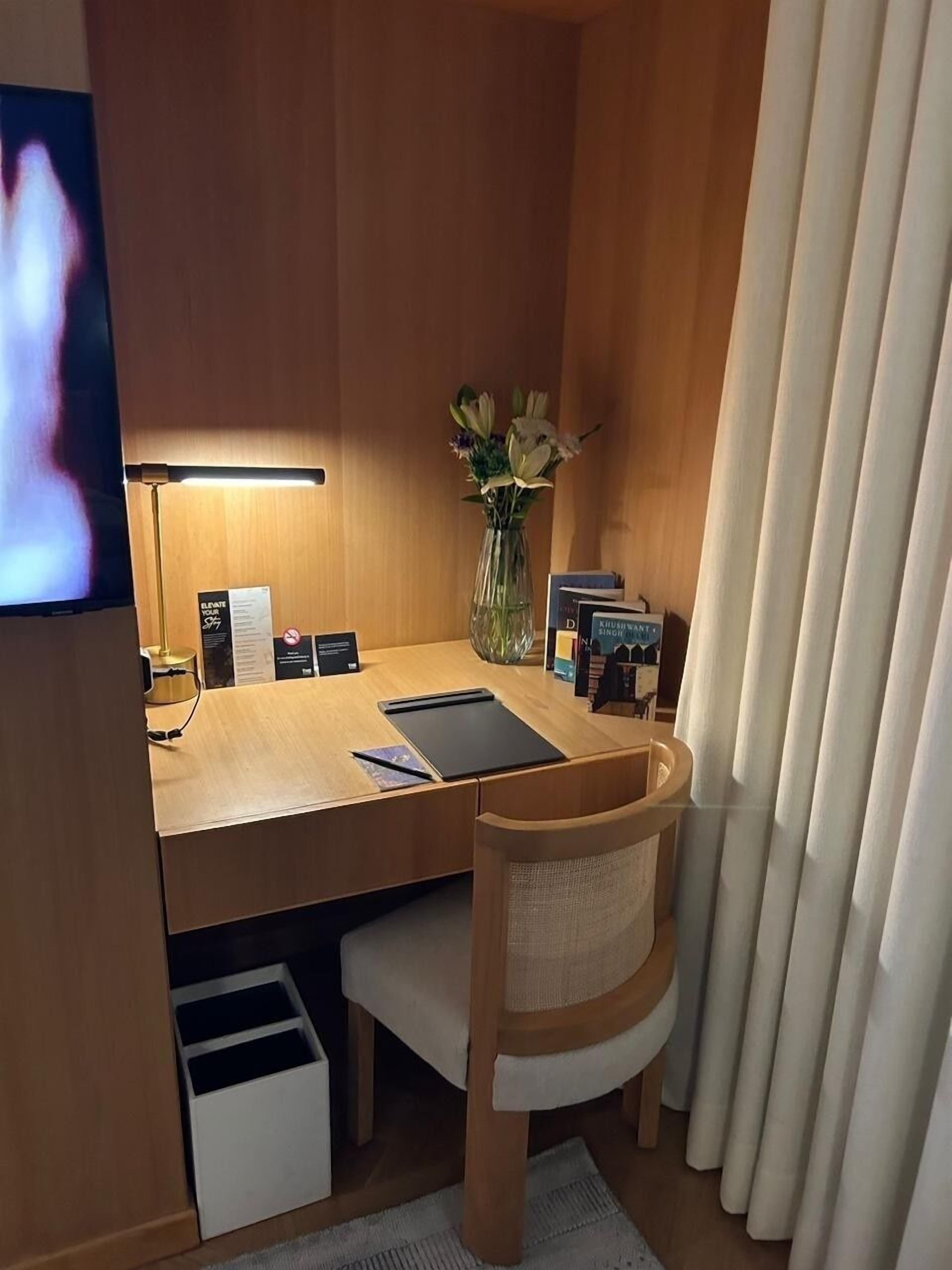 Een knus hotelkamer met een houten bureau, een stoel, een kleine vaas met bloemen, een lamp en een televisie.