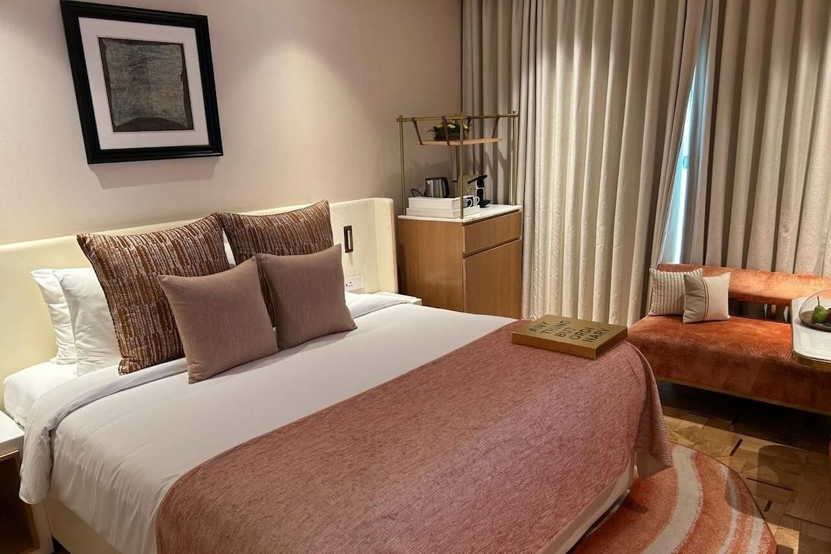 A neatly arranged hotel room with a large bed, a bedside table, a small desk, and a sofa.