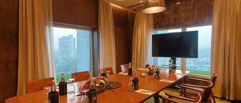 A conference room with a long table, chairs, a TV, and a city view.
