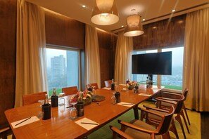 Sala de conferência com uma mesa comprida, cadeiras, uma televisão e vista para a cidade.