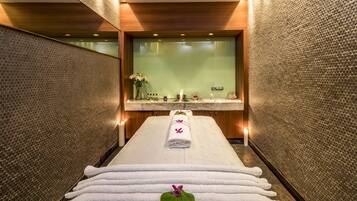 Relax in a serene spa room with a central bench, neatly folded towels, and decorative flowers.