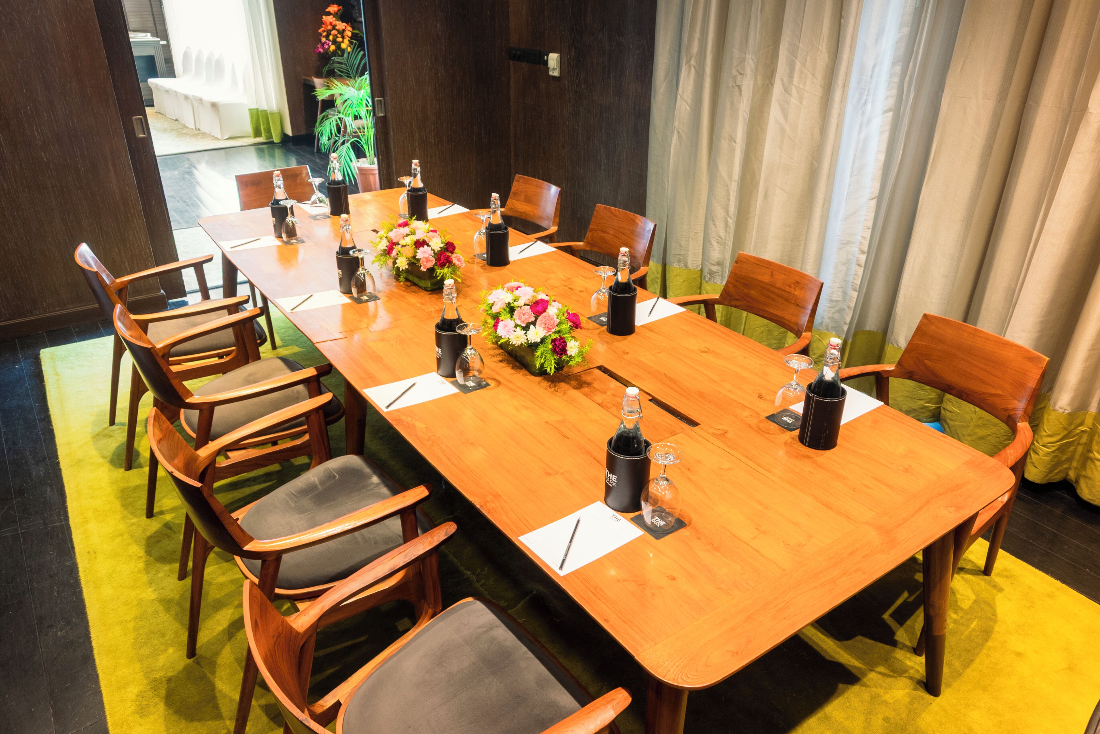 Un salón de conferencias con una larga mesa de madera, varias sillas y centros de mesa con flores.