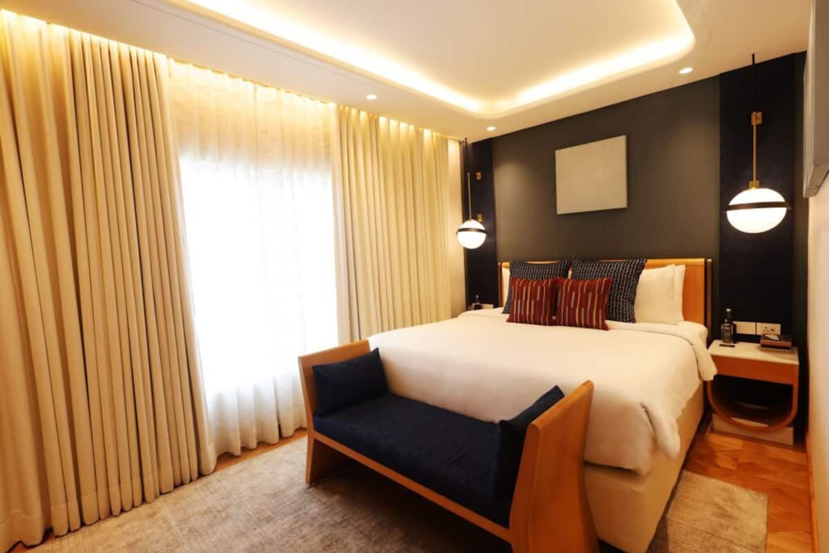 A modern hotel room with a large bed, bedside tables, a sofa, and a large window with curtains.