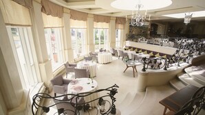 A spacious, elegantly decorated lounge area with multiple seating options, including round tables and cushioned chairs, and a curved balcony with a wrought iron railing. - The Vineyard (Newbury)