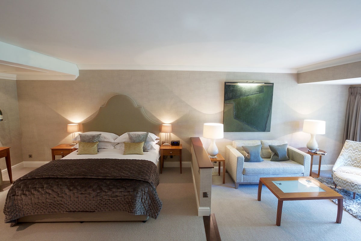 A hotel room with a large bed, a sofa, a coffee table, and a painting on the wall.