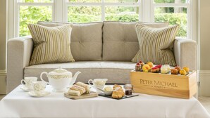 A cozy seating area with a cushioned sofa, a table with tea set and pastries, and a wooden crate labeled "Peter Michael Winery." - The Vineyard (Newbury)