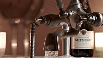Un grifo metálico con agua corriendo, una botella de champán Taittinger y un fondo desenfocado.
