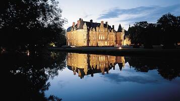 A large, historic building with a symmetrical facade and multiple towers, reflected in a calm body of water.