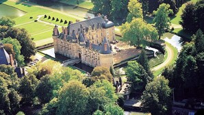 Een groot, historisch gebouw met meerdere torens, omgeven door weelderige begroeiing en een verzorgd gazon.