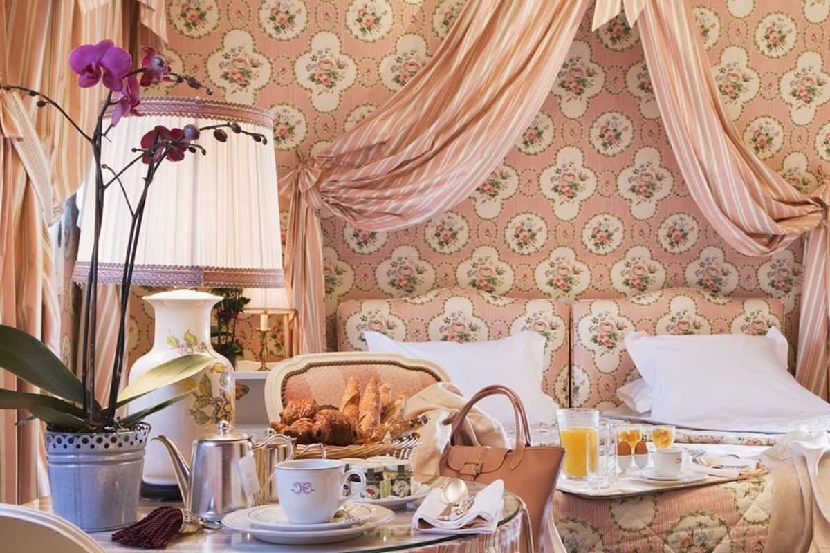 A room with a bed, a dining table with breakfast items, a potted plant, and a nightstand with a lamp.