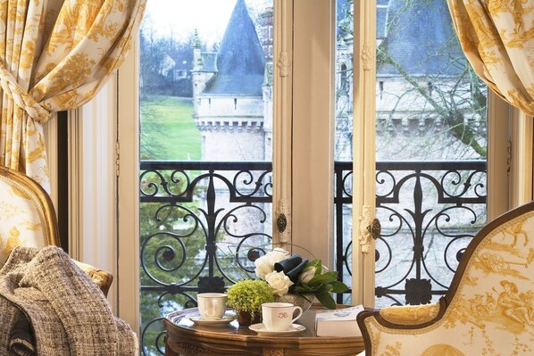 Un balcón con barandillas de hierro forjado decorativas, una mesa con un florero y vistas a un castillo.