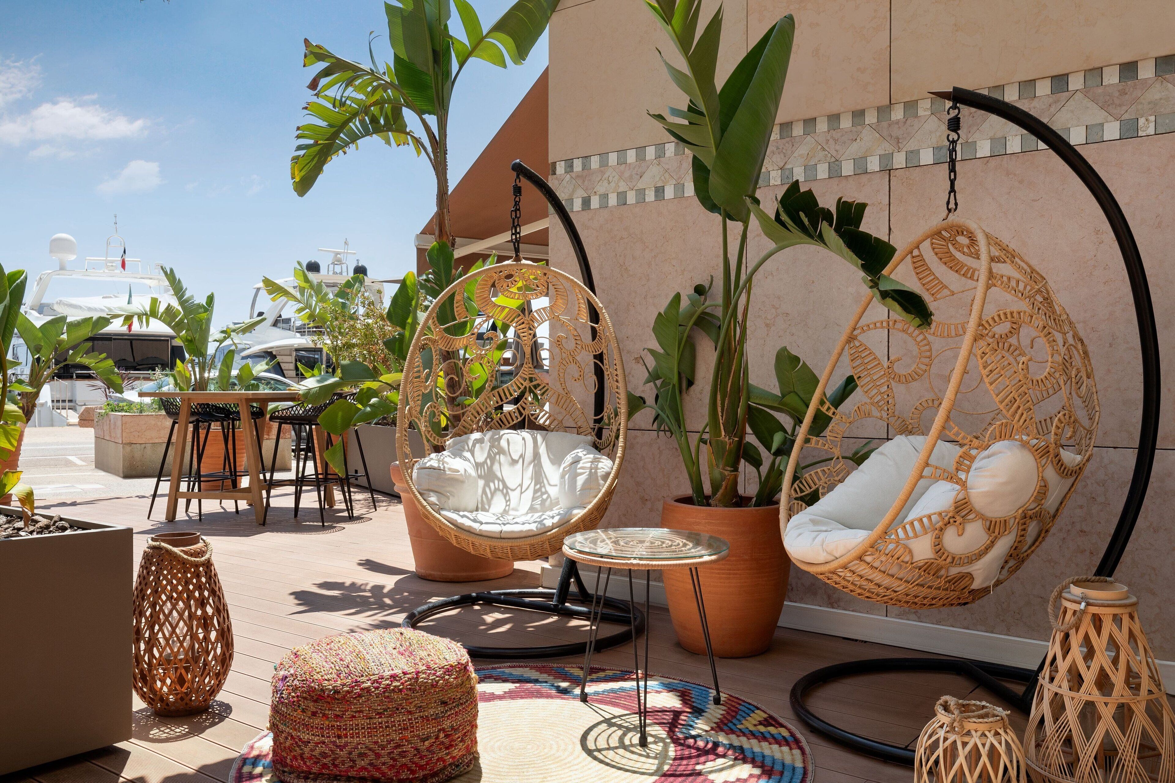 A rooftop terrace with wicker hanging chairs, a round table, and potted plants.