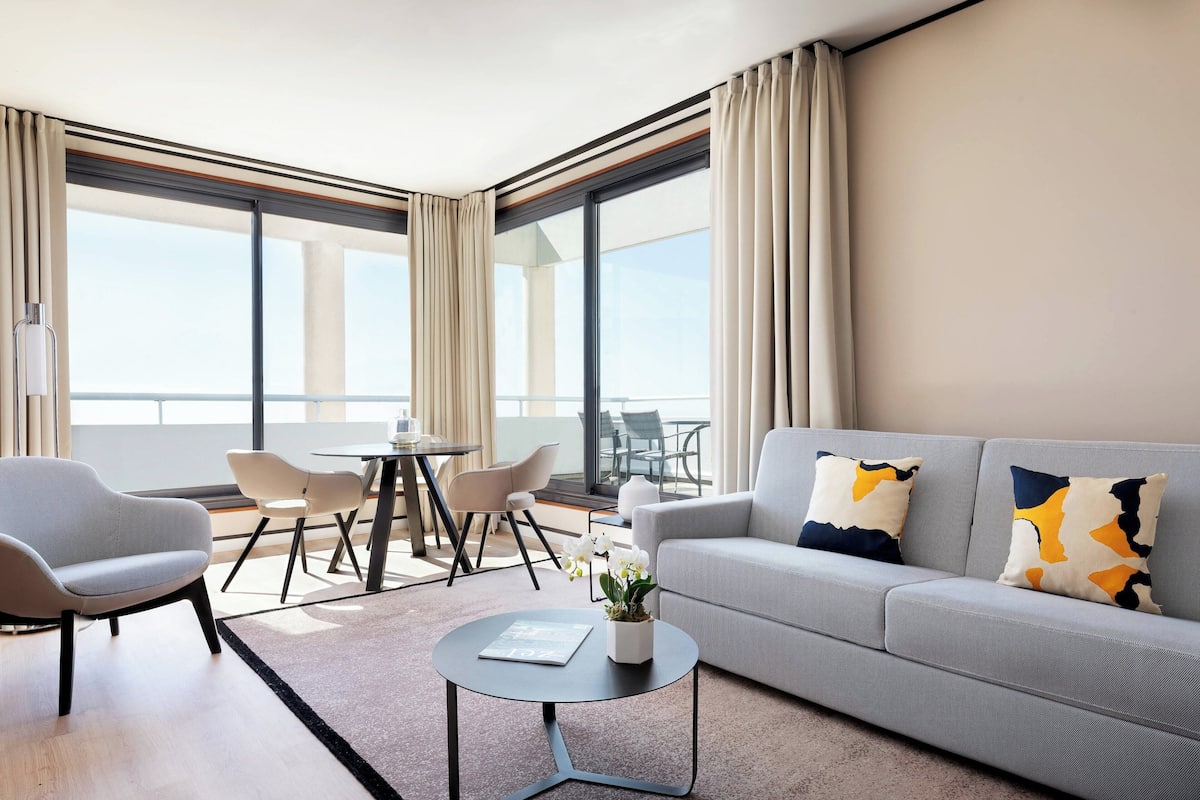 Un salon moderne avec un canapé gris, deux fauteuils, une table basse ronde et un coin repas comprenant une table et des chaises.