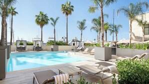 Un área de piscina con sillones de descanso y palmeras.