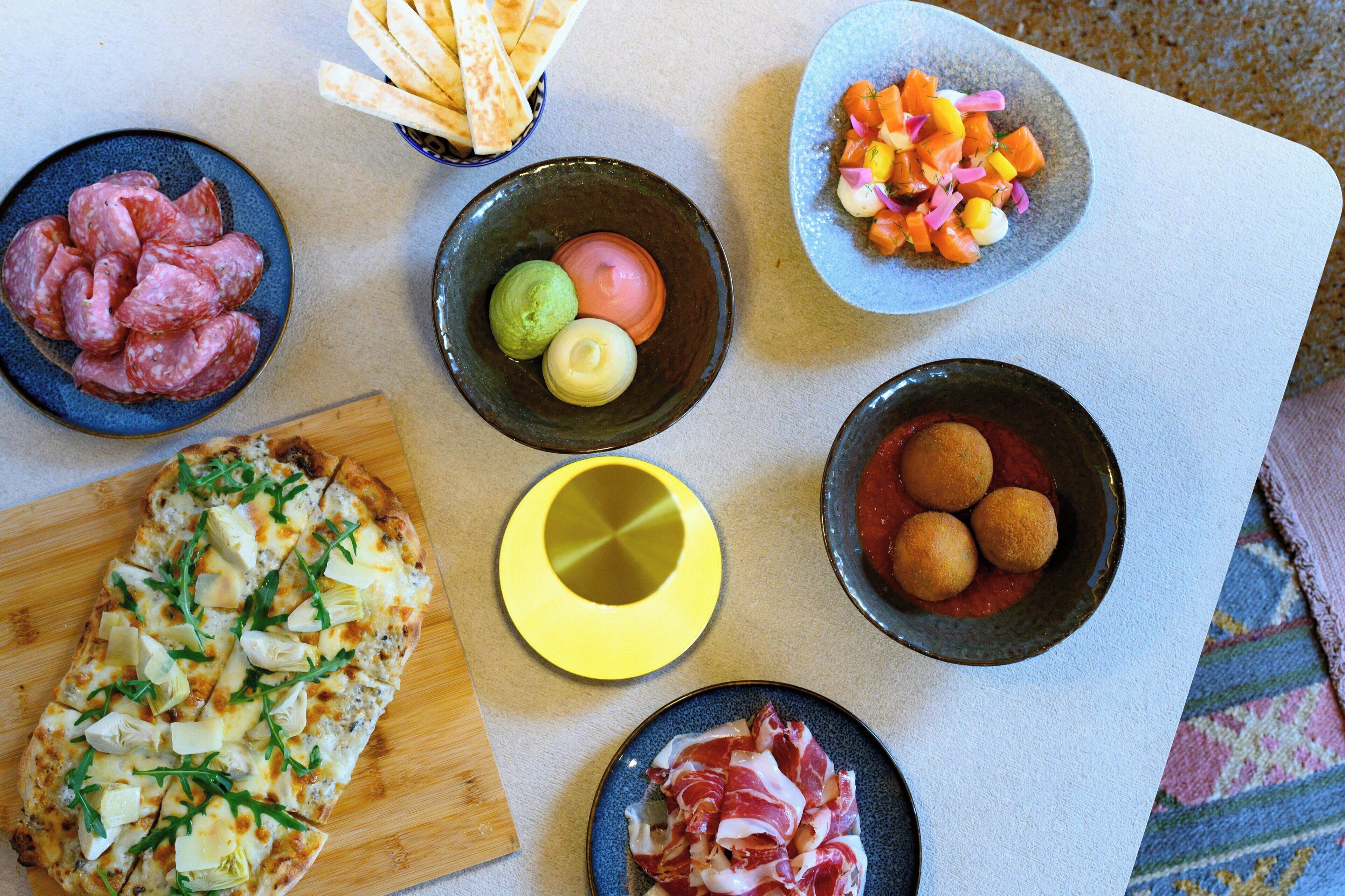 Een tafel met diverse etenswaren, waaronder pizza, vlees en een fruitsalade.