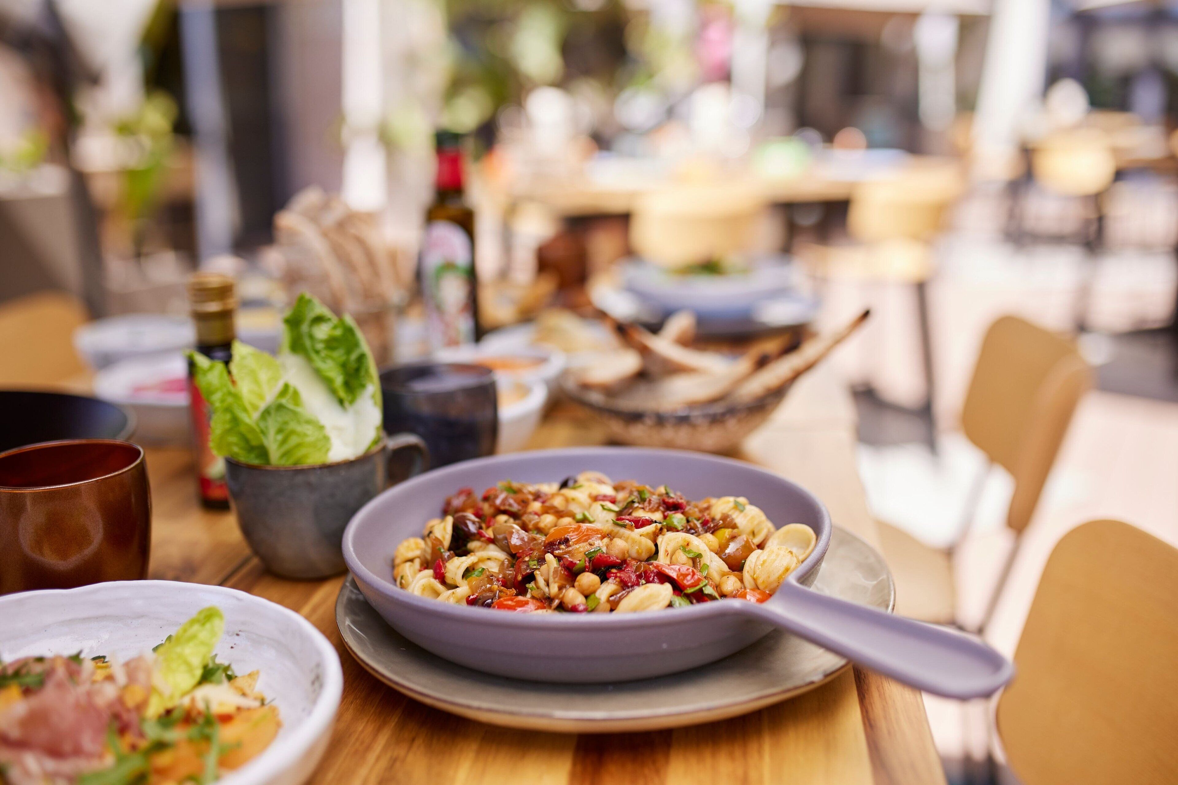Une table à manger avec un bol de pâtes, une tasse et un petit bol de légumes verts.