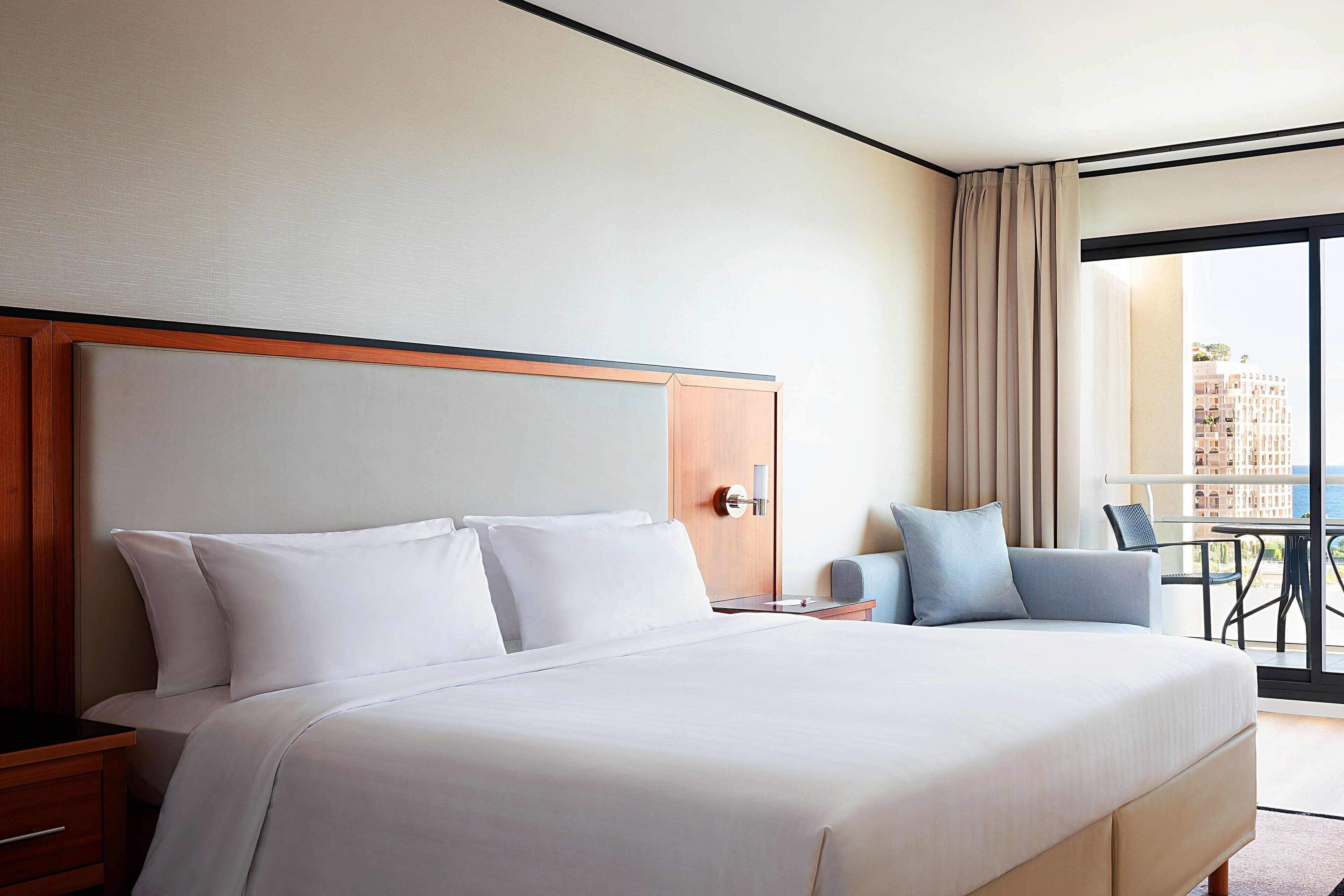 Une chambre d’hôtel avec un grand lit, une tête de lit en bois, une table de chevet, un bureau et une vue sur la ville par une grande fenêtre.