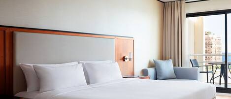 Une chambre d’hôtel avec un grand lit, une tête de lit en bois, une table de chevet, un bureau et une vue sur la ville par une grande fenêtre.