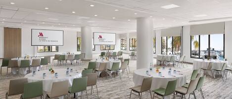 A spacious conference room with multiple round tables and chairs, large windows with a view of the city, and a clean, modern design.