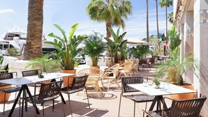 Un patio al aire libre con mesas y sillas, rodeado de palmeras y plantas en macetas.