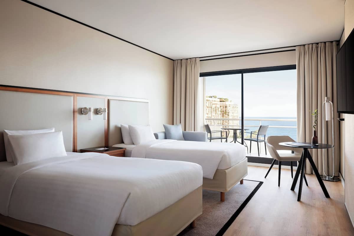 Une chambre d’hôtel avec deux lits, un bureau, une chaise et une vue sur la mer.