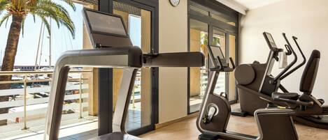 A gym with treadmills and elliptical machines, large windows with a view of palm trees and a parking area.