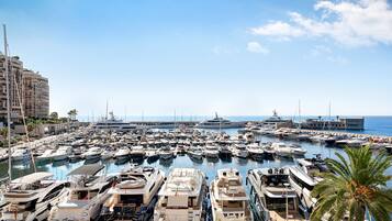 Un port de plaisance où sont amarrés de nombreux bateaux, ainsi qu’un grand yacht et un immeuble doté de balcons.