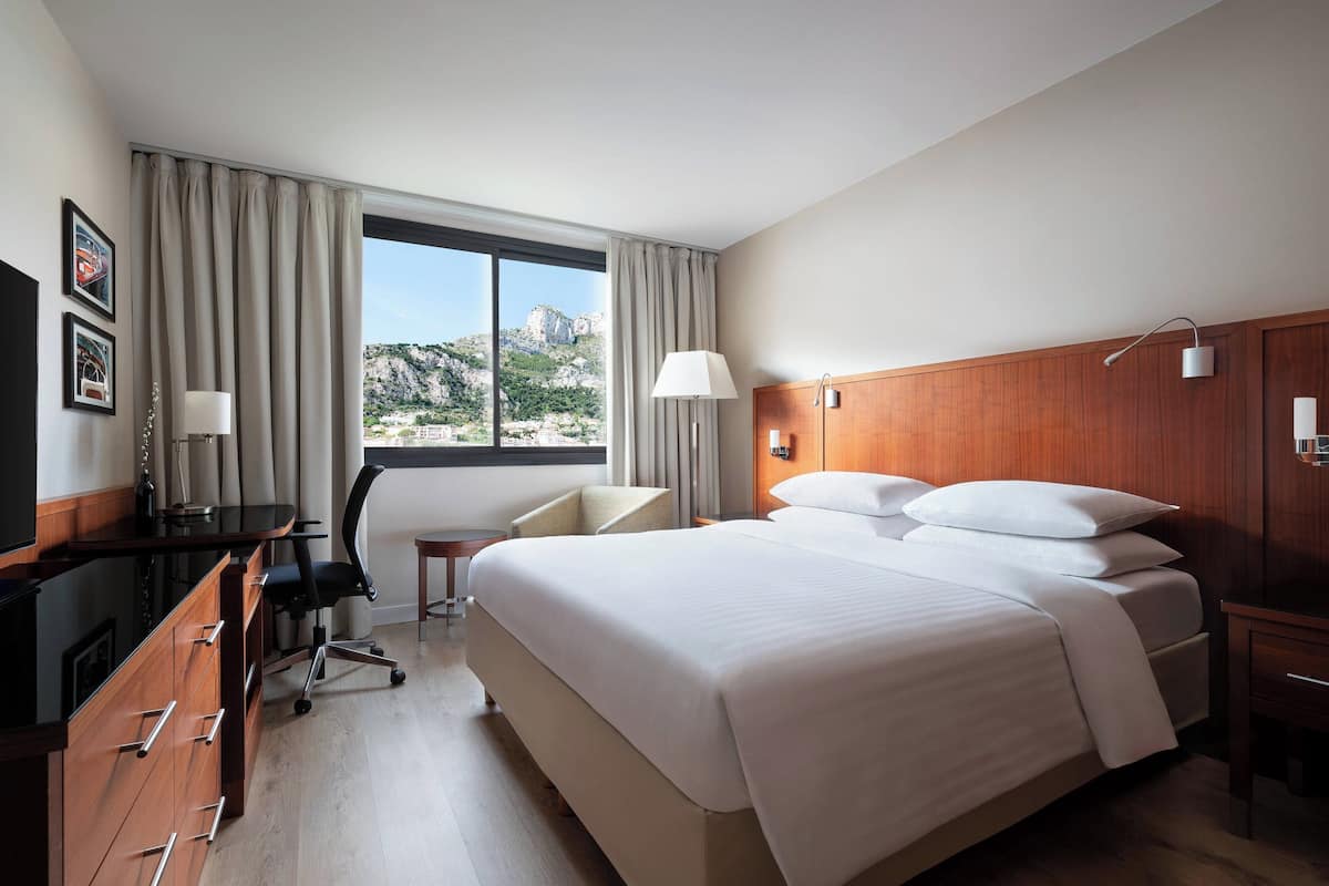 Une chambre d’hôtel avec un grand lit, un bureau avec une chaise, une télévision et une vue sur un paysage montagneux.