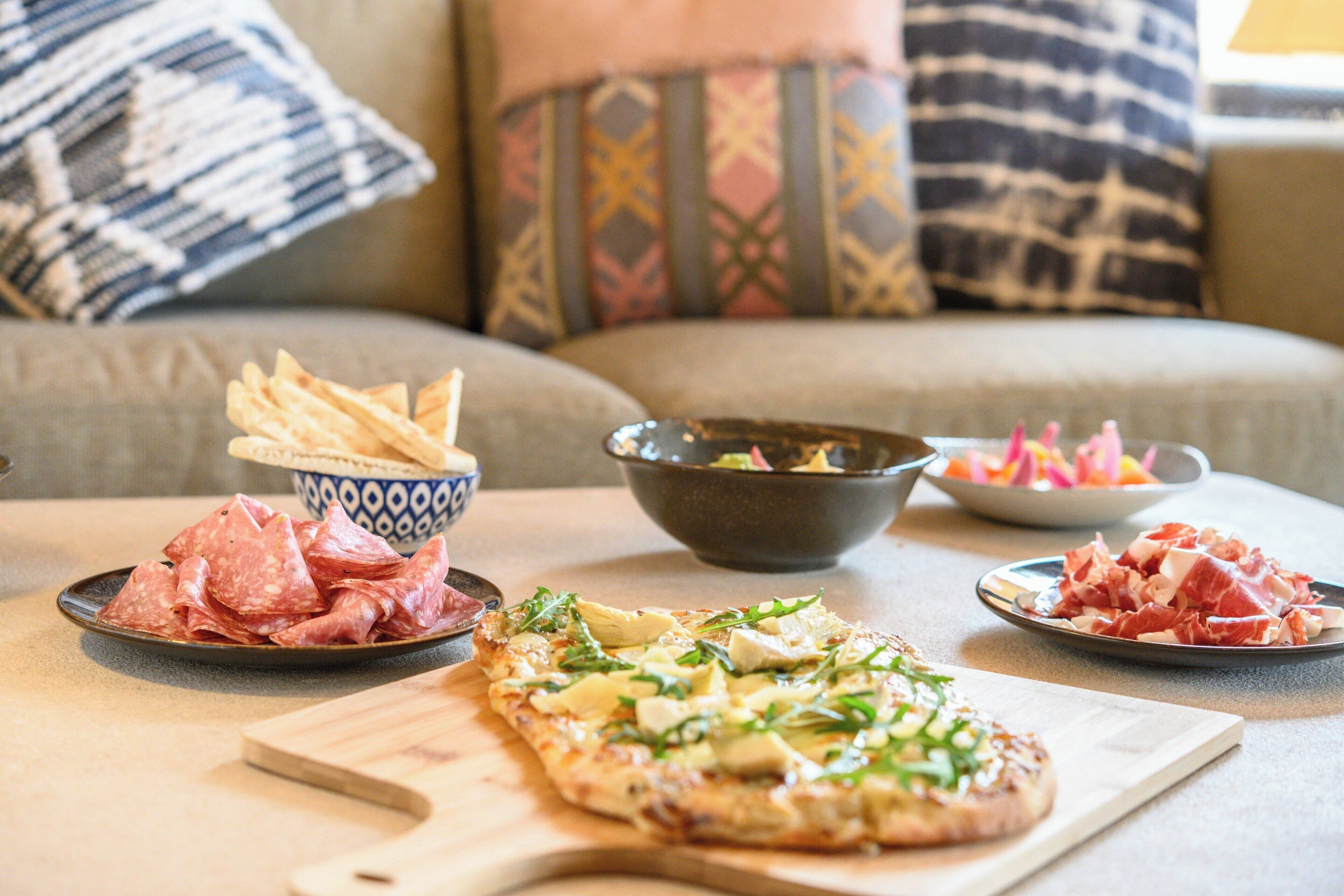 A dining table with a pizza, bowls of food, and plates of meat.