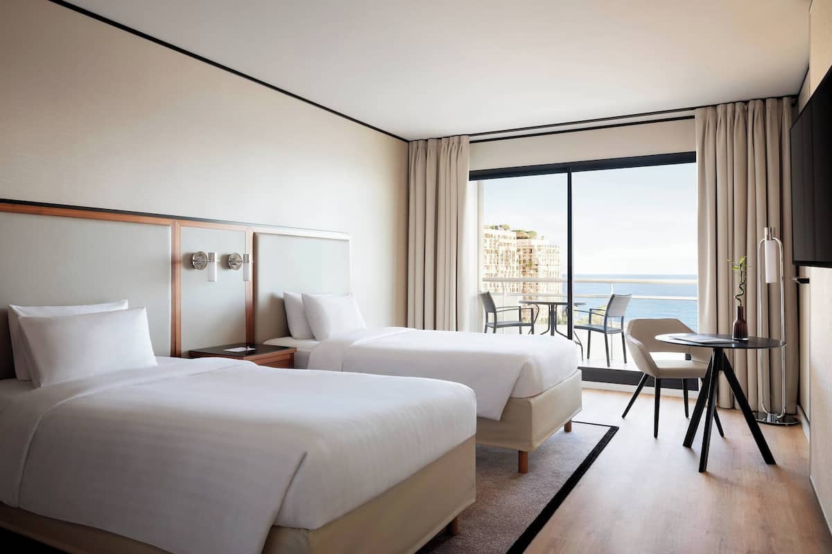 Une chambre d’hôtel avec deux lits, un bureau, une chaise et une vue sur la mer.