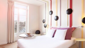 Une chambre d’hôtel avec un lit, une table ronde, une vue sur un pont et une fenêtre avec des rideaux.