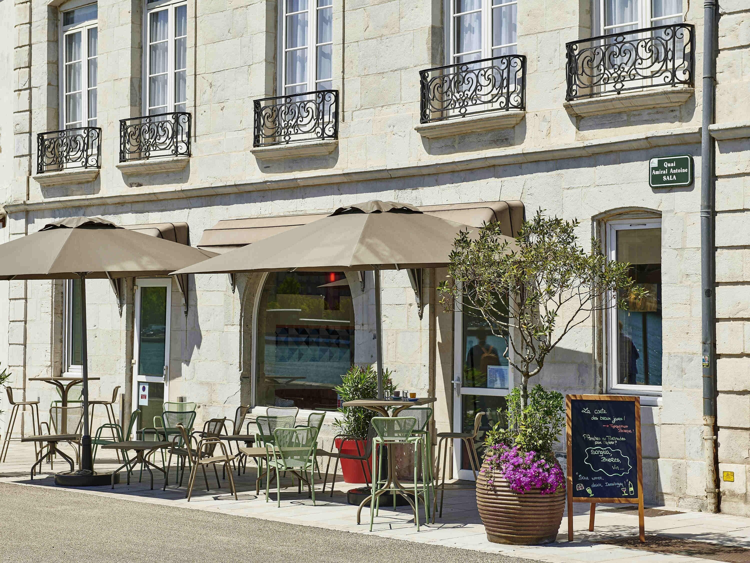 A cafe with outdoor seating, a chalkboard menu, and a sign indicating the name 'Quai Amiral Antoine Sala'.