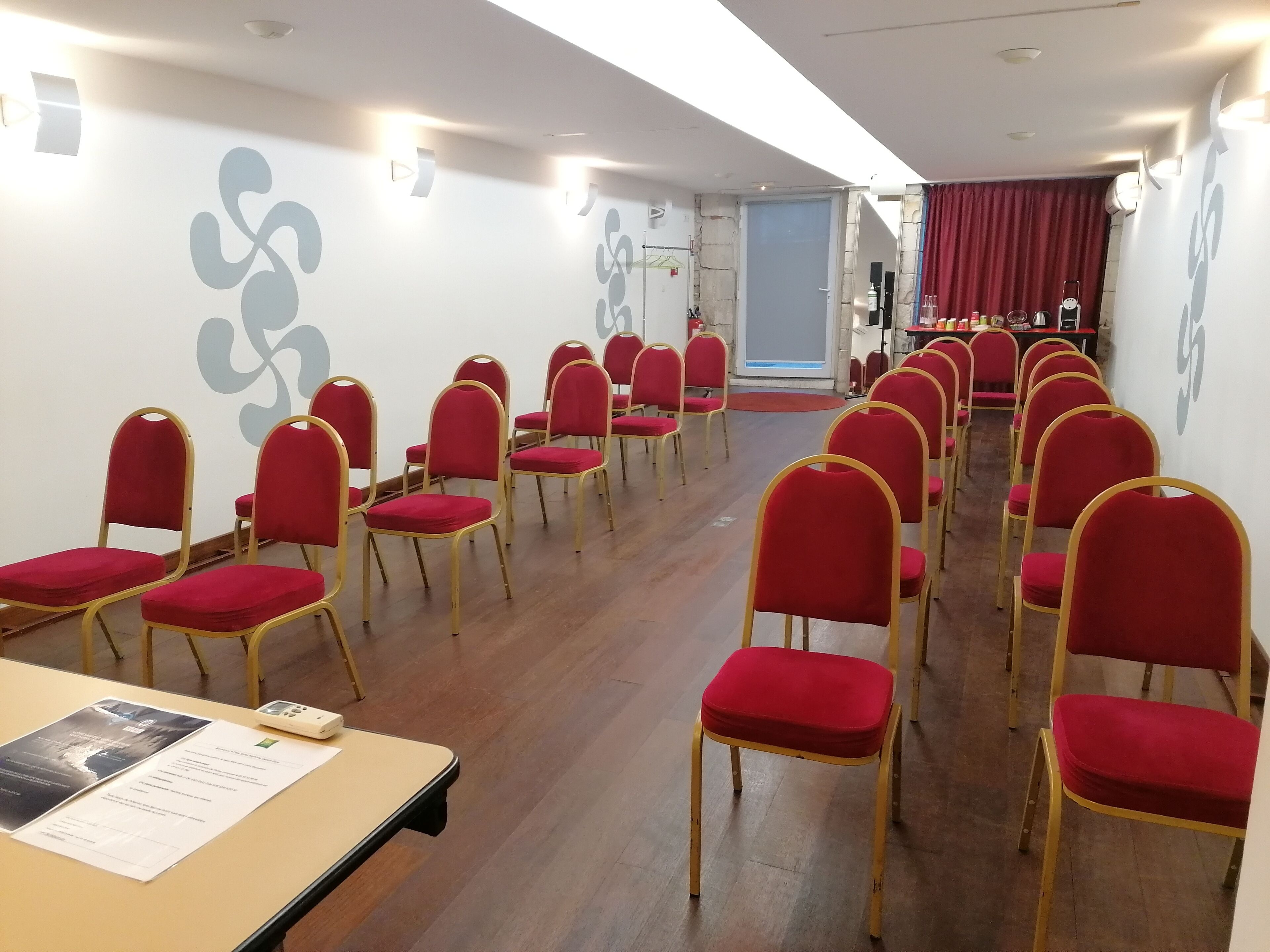 A conference room with rows of red chairs and a table with documents.