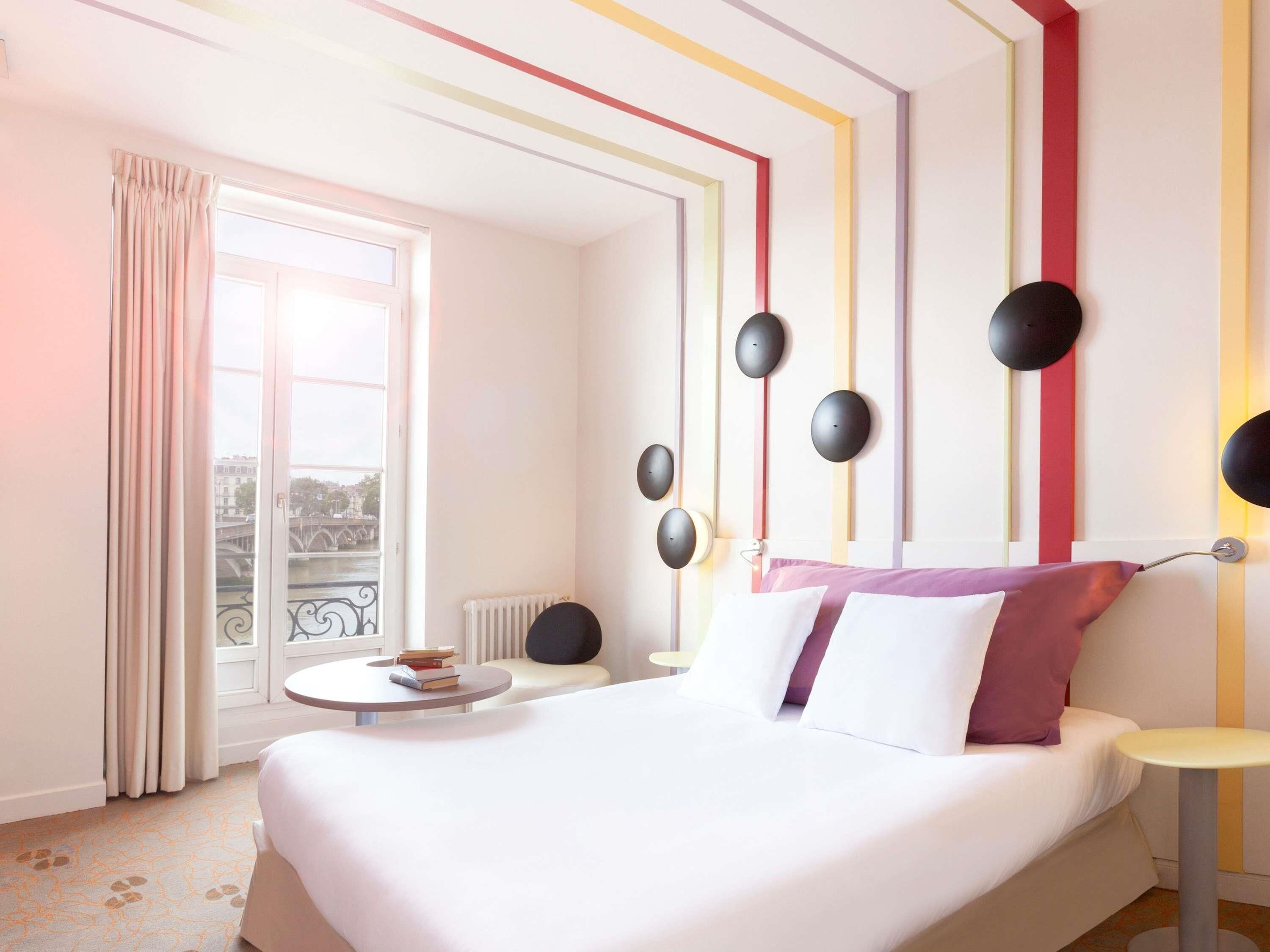 Una habitación de hotel con cama, una mesa redonda, una ventana con cortinas y vista a un puente.