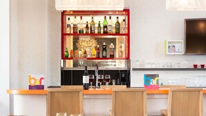 Un espace bar avec un assortiment de bouteilles d’alcool, une machine à café et un téléviseur fixé au mur.