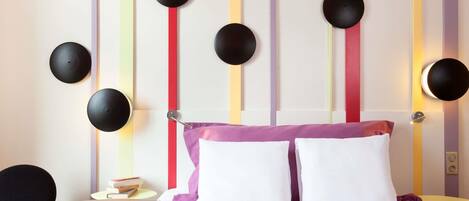 Una habitación de hotel con cama, mesitas de noche, una silla y una estantería.
