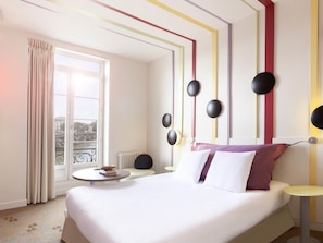 Habitación de hotel con cama, mesitas de noche, ventana con cortinas y vistas a un puente, además de un radiador.